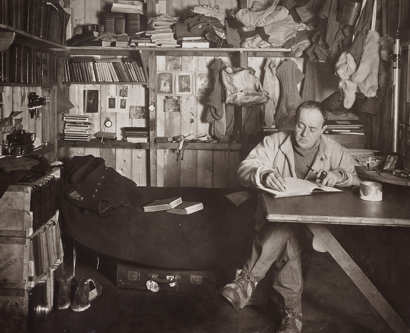 Scott escribiendo su diario en la cabaña del cabo Evans durante el invierno de 1911. Fotografía de Herbert Ponting.